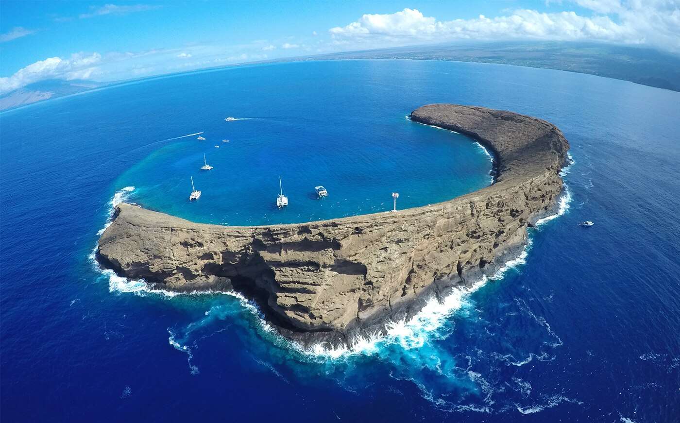 Aerial view of Molokini's crescent rim with snorkel boats anchored in the clear crater water